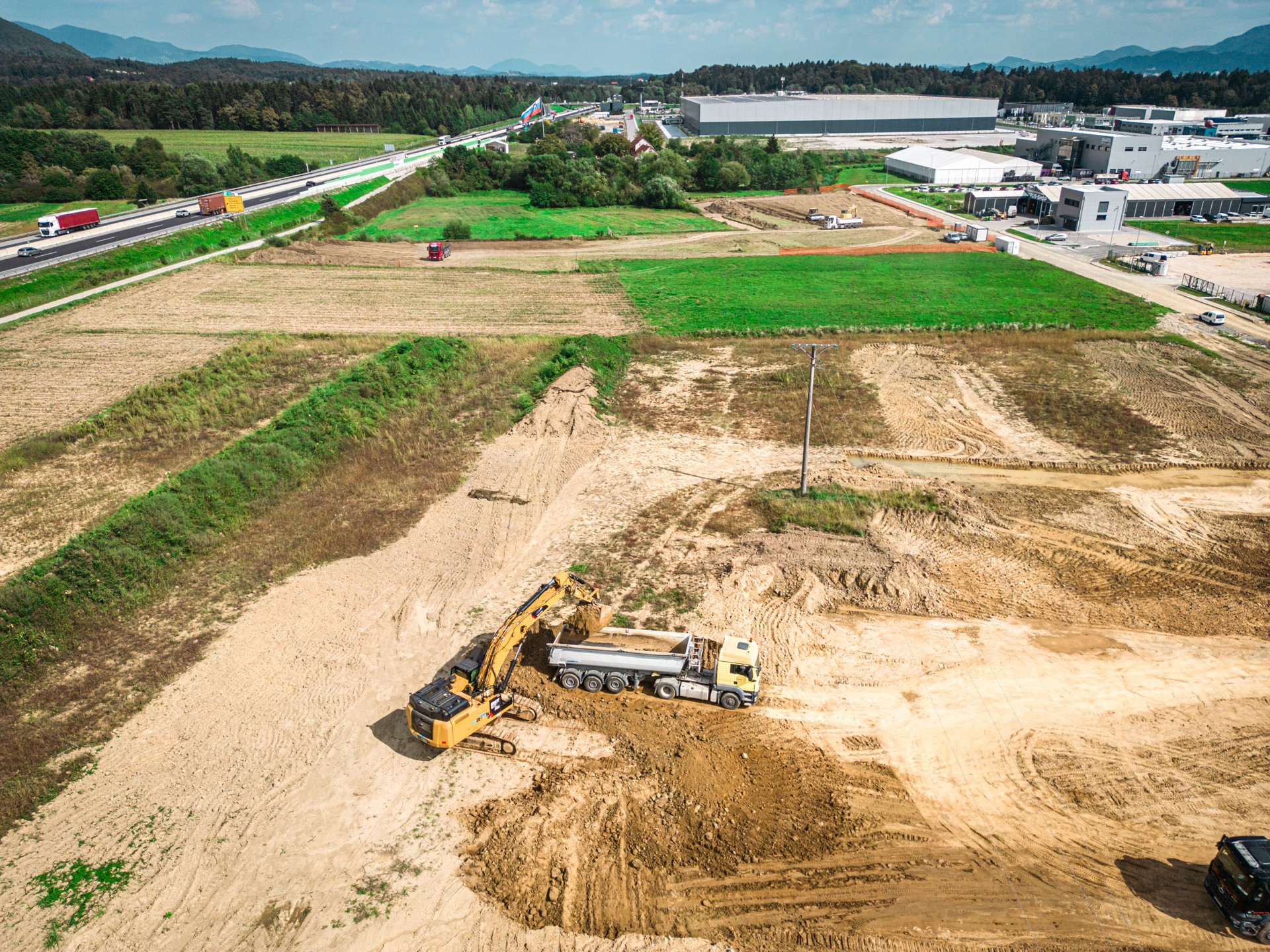 Large excavator loading piles of dirt and material on dump trucks
